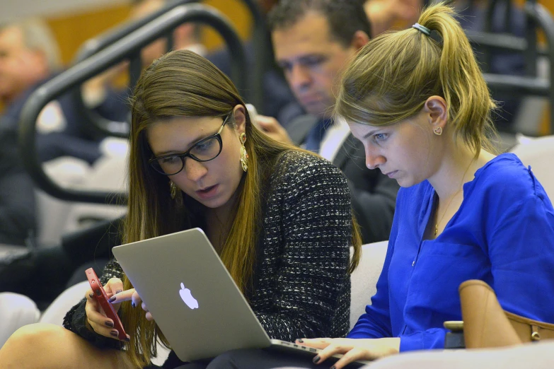 two young women using a lap top in a crowded room