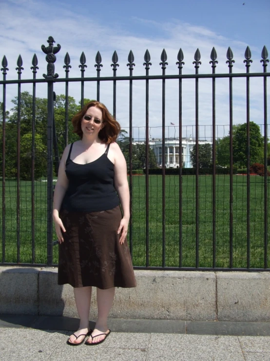 a woman in sunglasses standing next to a fence