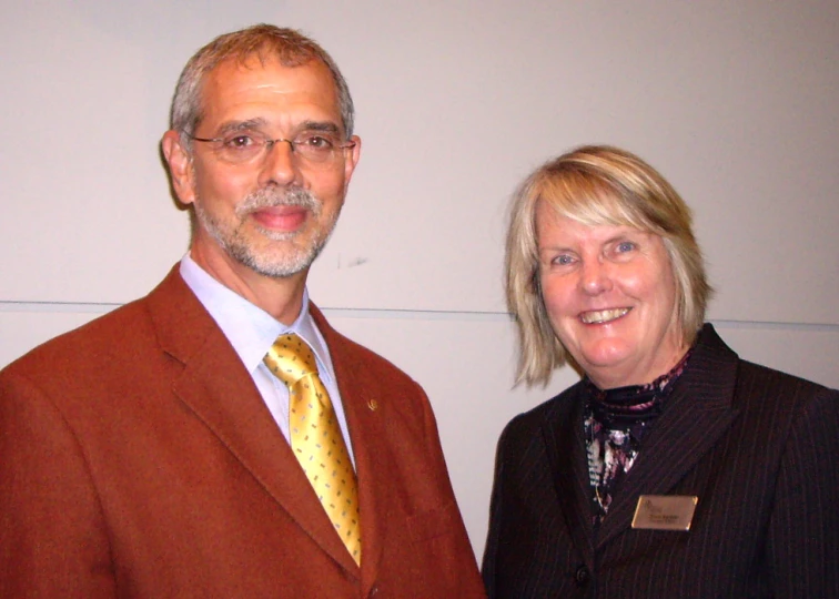 the two people smile together near a white wall