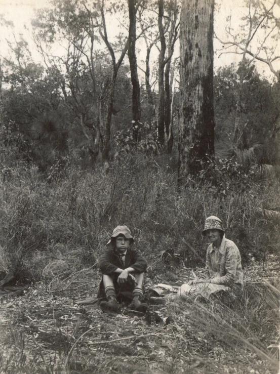two men sit in the woods on the ground