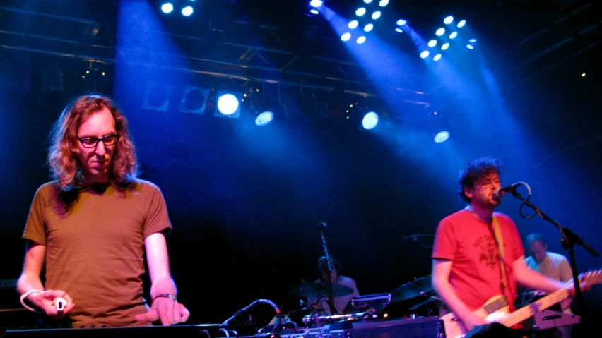 three people with guitar standing in front of purple and blue lighting