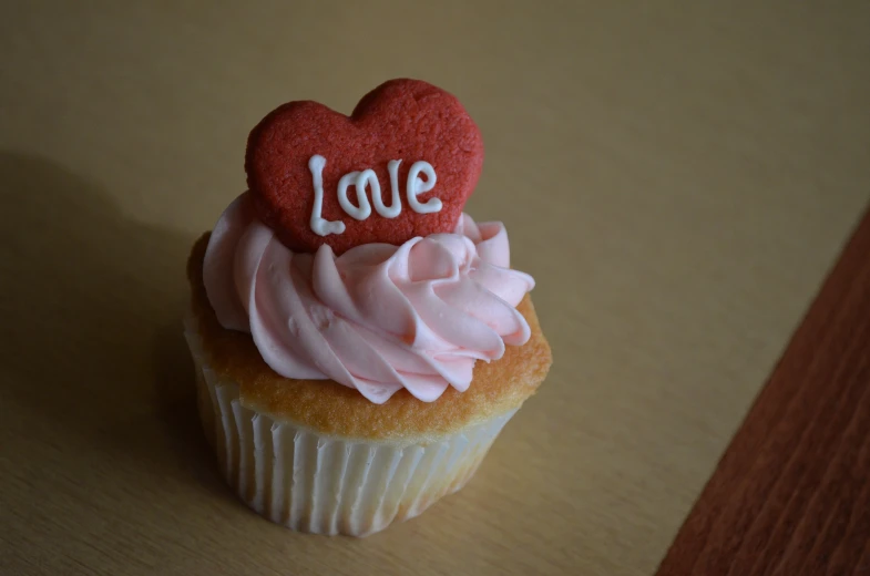 a cupcake topped with pink frosting with an icing heart shaped love spelled with the word love