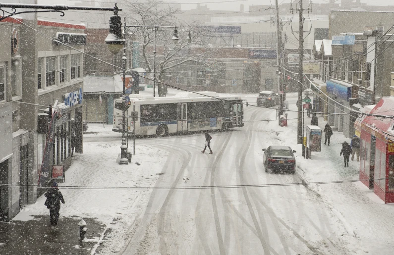 city street with cars, buses and people in the snow