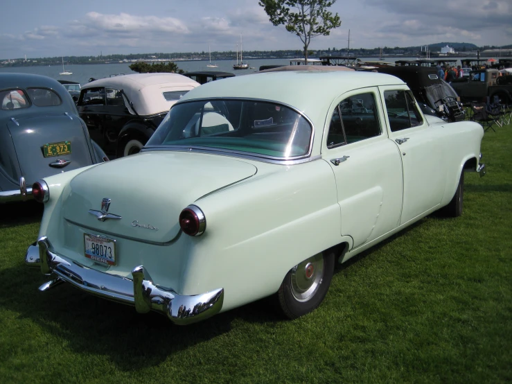 a light blue classic car parked in the grass at a car show