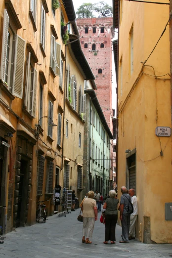 several people walking down a narrow alleyway between yellow buildings
