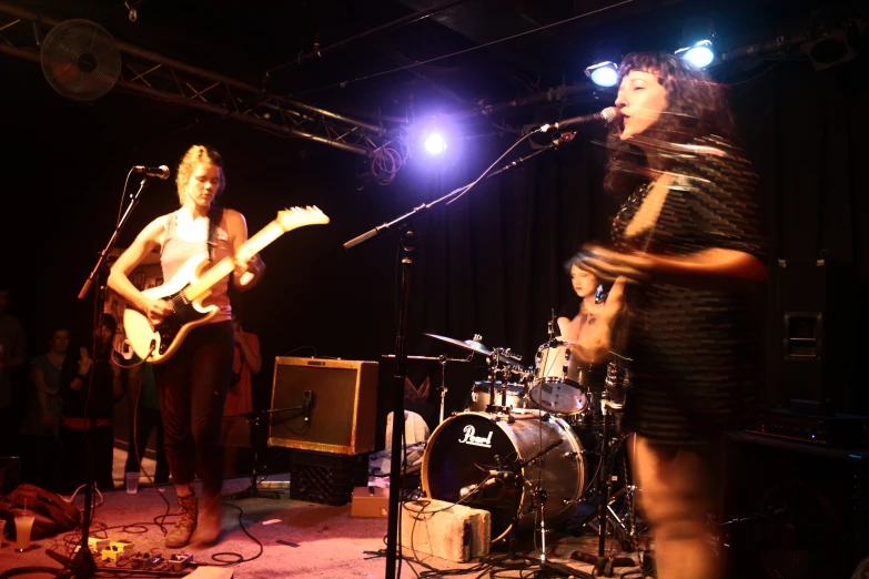 two women singing on stage with a man playing guitar