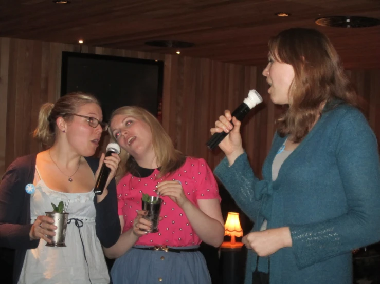 three young ladies drinking and singing into microphones