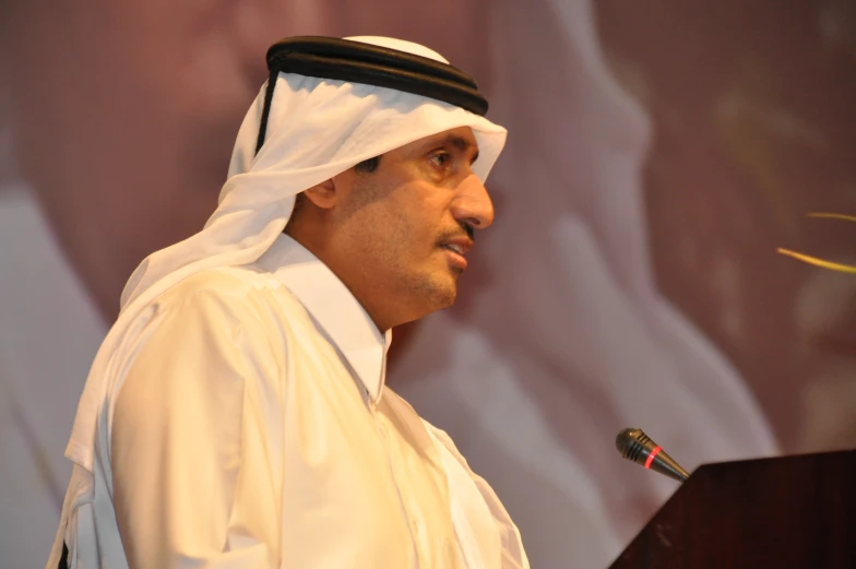 a man dressed in white and head covering standing at a podium