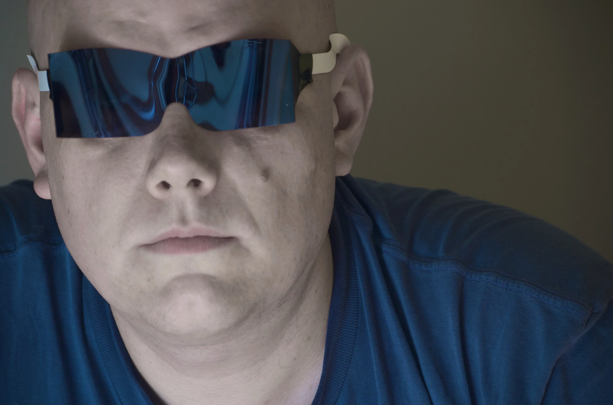 man with blue shirt and eye patch looking down with small glasses on his eyes