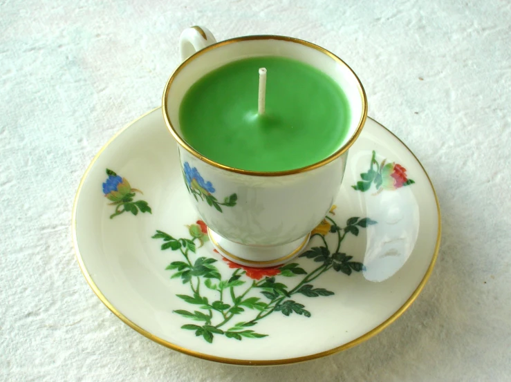 a white cup with green liquid and a candle in the cup