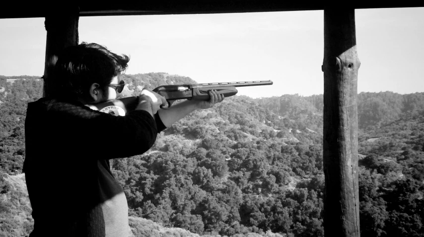 a man holding a gun up to the sky with a forest in the background