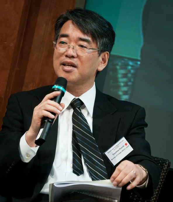 asian man in suit and tie sitting down with microphone