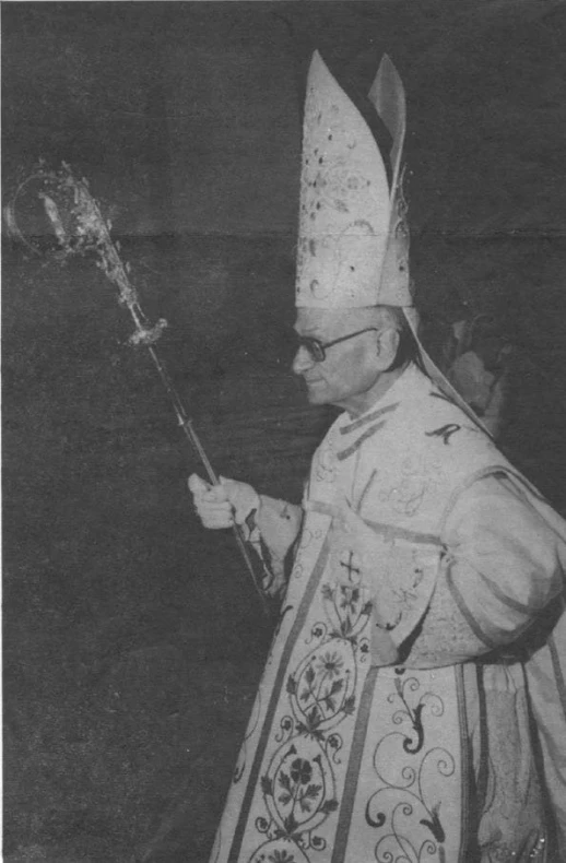 a man wearing a priest's uniform holds up an iron cross