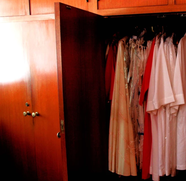 a wooden closet with several different clothes and jackets hanging on hooks