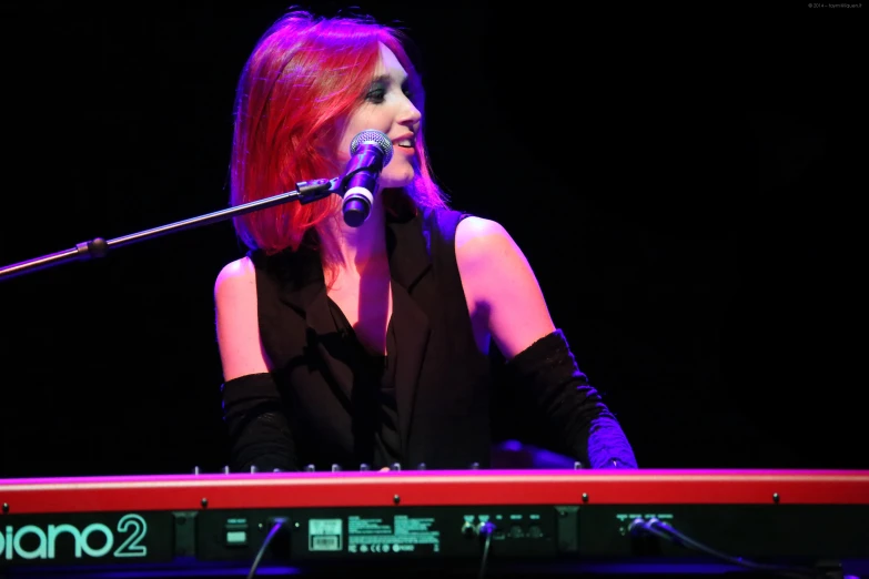 a woman wearing black, standing at a keyboard with microphone in front of her