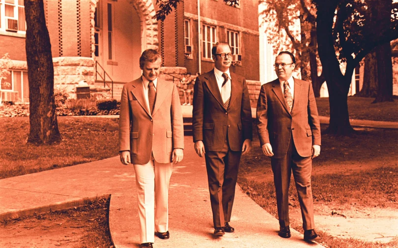 three men walking down the sidewalk while wearing suits