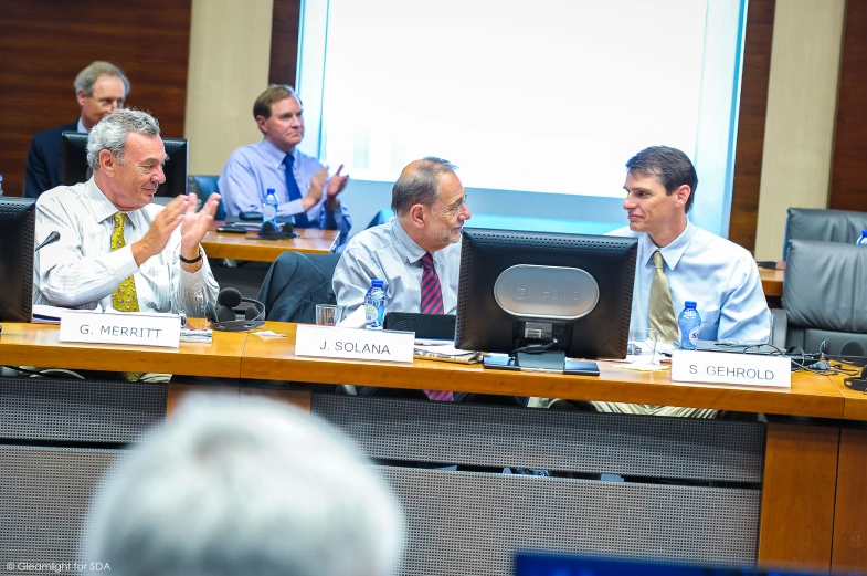 three men at a meeting one holding up his hand