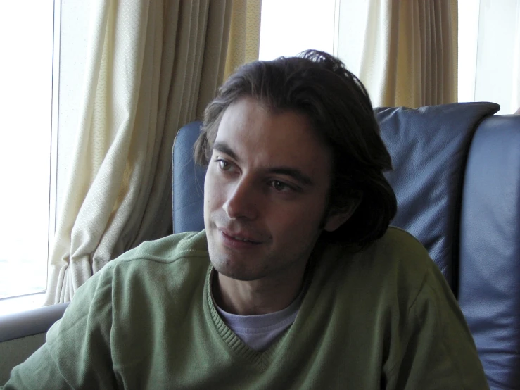 a man in green shirt with long hair next to window