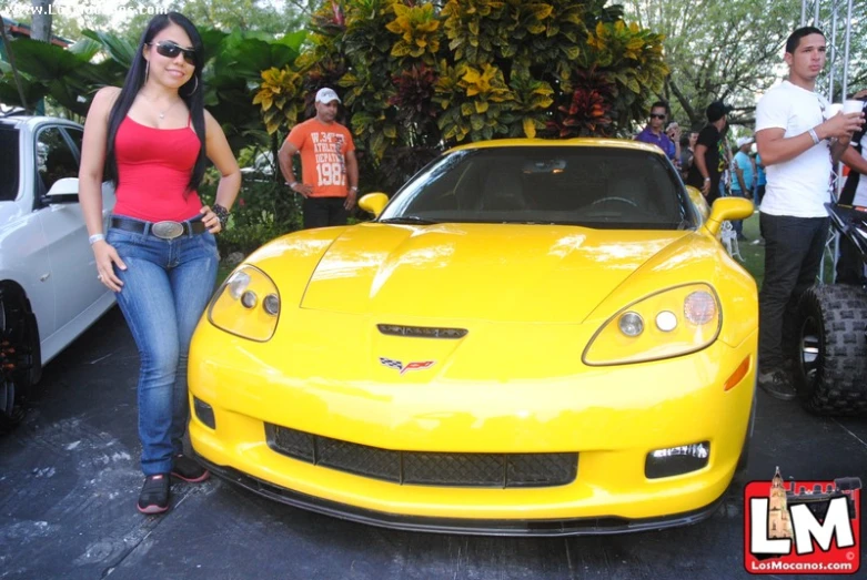 a woman in blue jeans and red top standing next to a yellow car