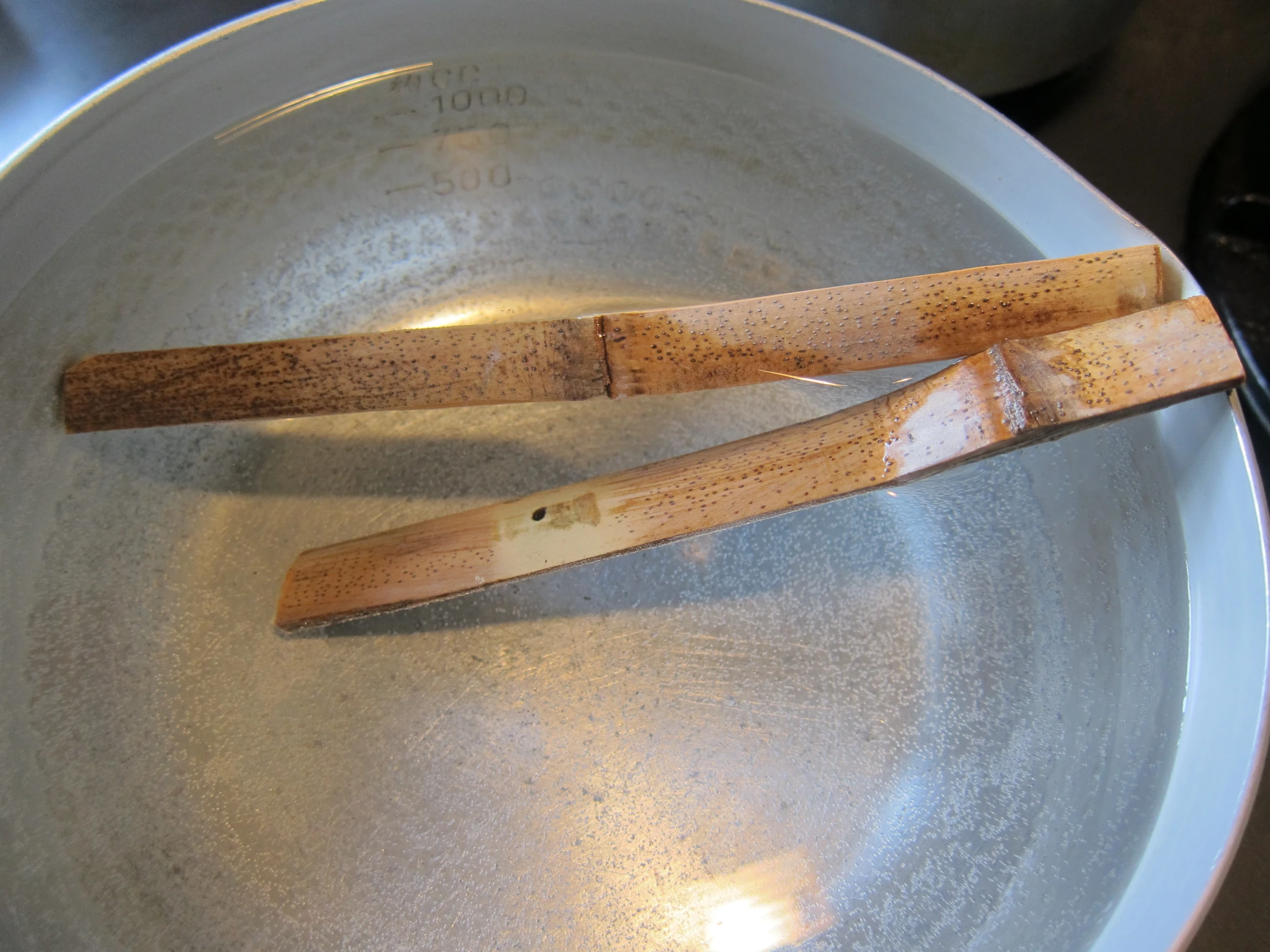 a metal pan with two wooden tongs in it