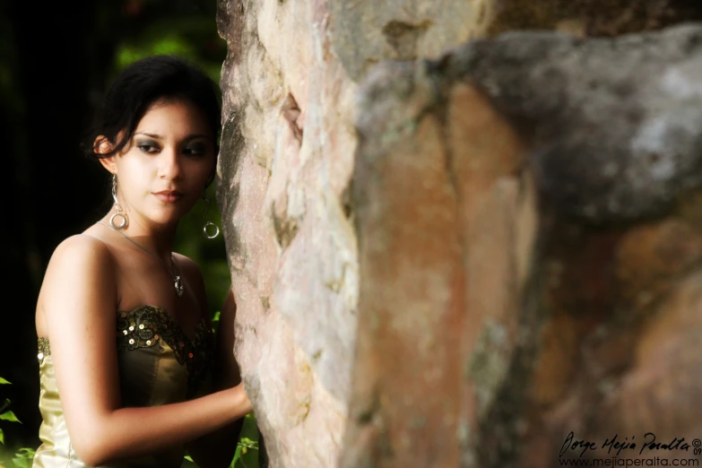 a beautiful young lady leaning against a stone wall