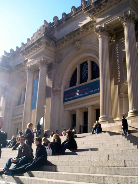 several people sit on the stairs in front of an old building