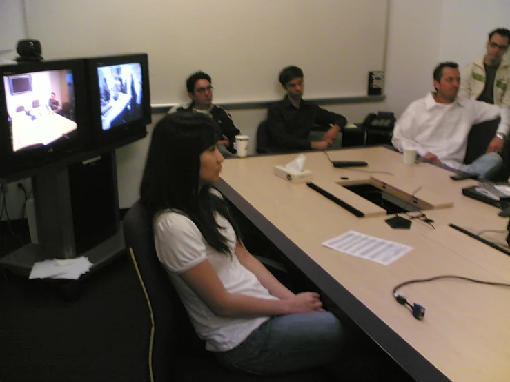 a group of people at a conference table in front of a television