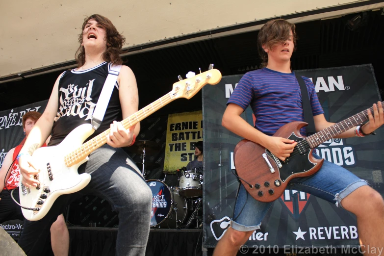 two young men with guitars stand in front of an outdoor stage