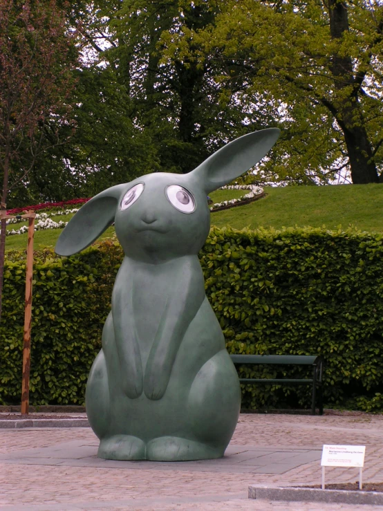 a sculpture of a large gray rabbit sitting in front of a tree