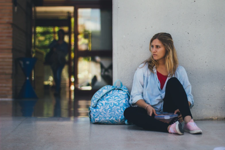 a woman sits on the ground with her backpack and shoes