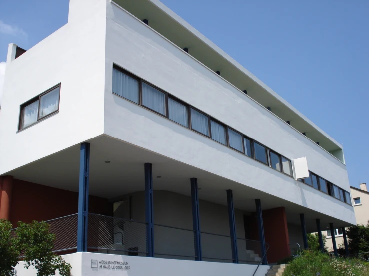 a white building with blue bars is next to an olive tree