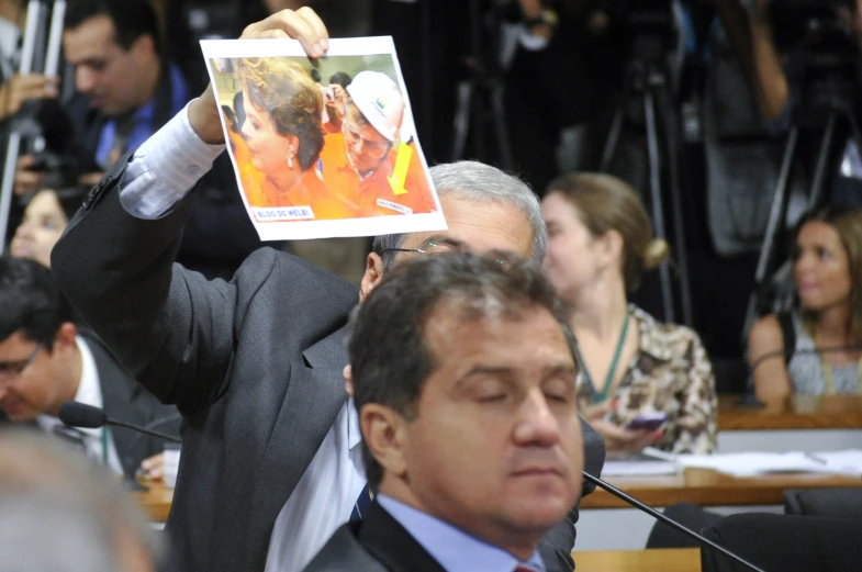 an audience watching a man in a suit holding up a po of his father