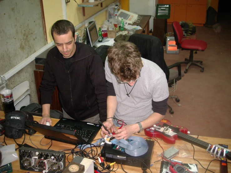 two men at a table looking at some electronics