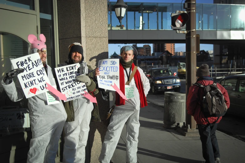 three men stand holding signs on a sidewalk