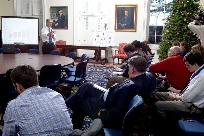 people are sitting in front of a board with a man at the podium