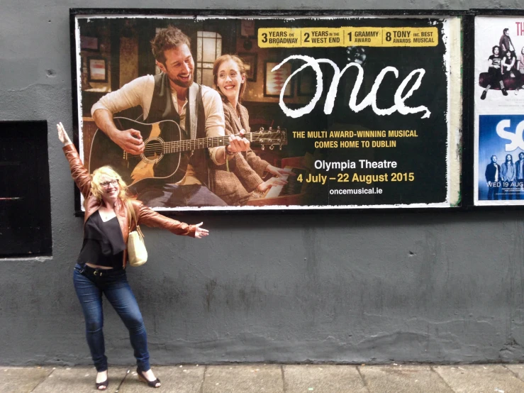 the woman stands in front of a posters advertising music