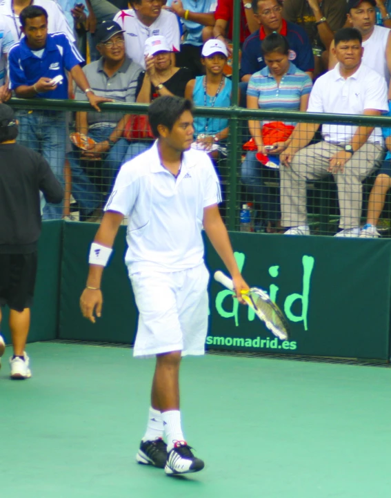 a man in all white playing tennis while a large crowd watches