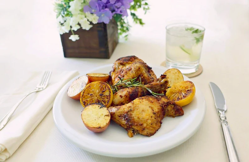 cooked meat with some garnish sitting on a plate with fork, silverware and glass