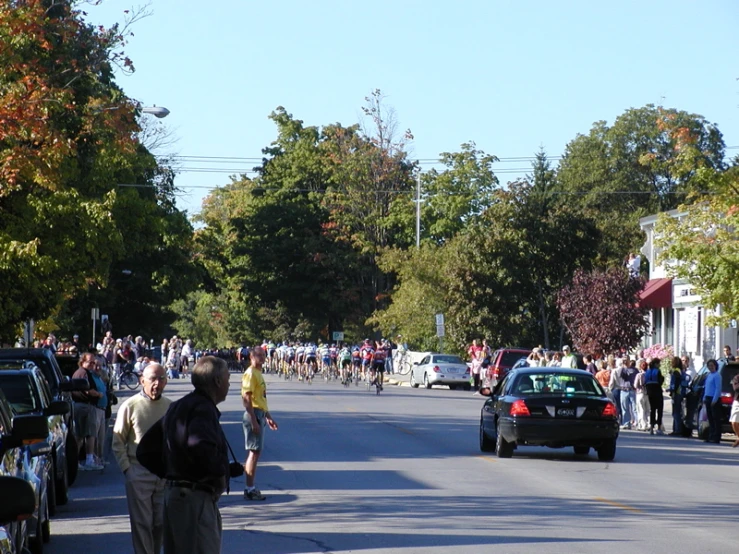 a group of people walk on the sidewalk, near parked cars