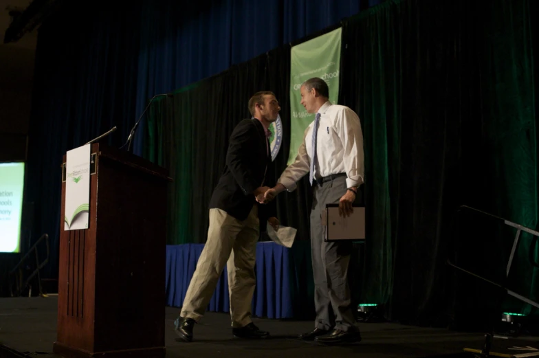 two men at podium with television behind them