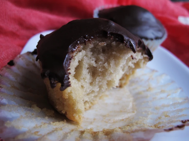 a half eaten chocolate covered donut on a paper plate