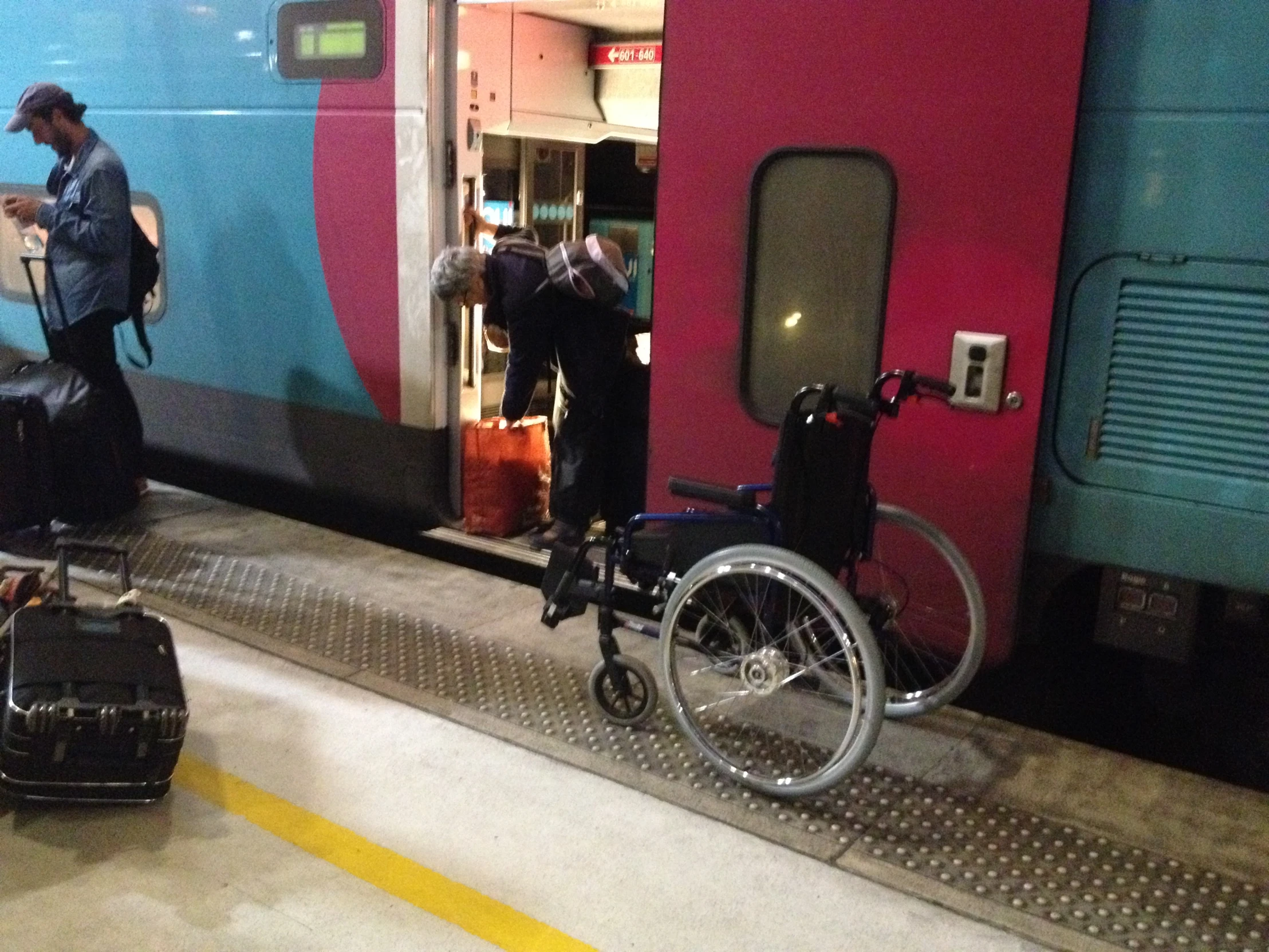 two people with luggage wait in front of a train