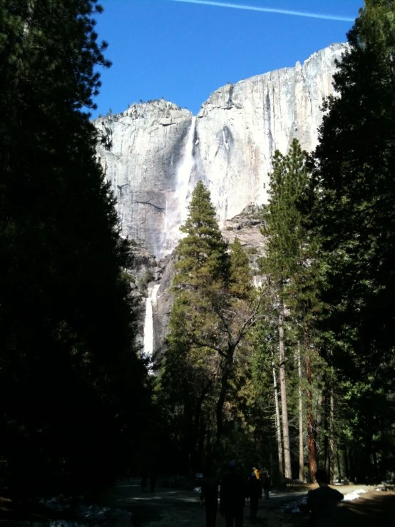 two people walking down a mountain road in front of a waterfall