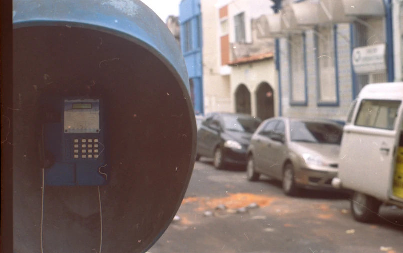 a parking meter is shown in the foreground and a couple of cars in the background