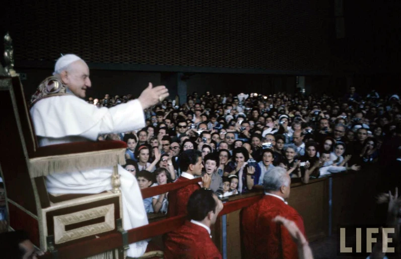 a man in white robes giving a speech to a group of people