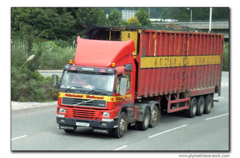 a red dump truck driving on the street next to trees