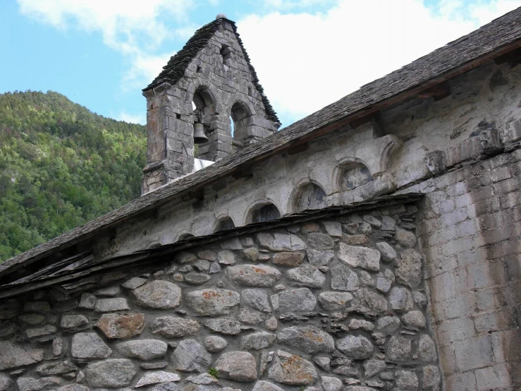 an old stone wall by a large building and mountains