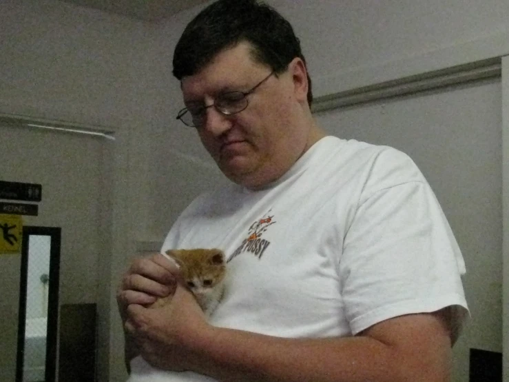 a man that is holding a kitten and wearing glasses