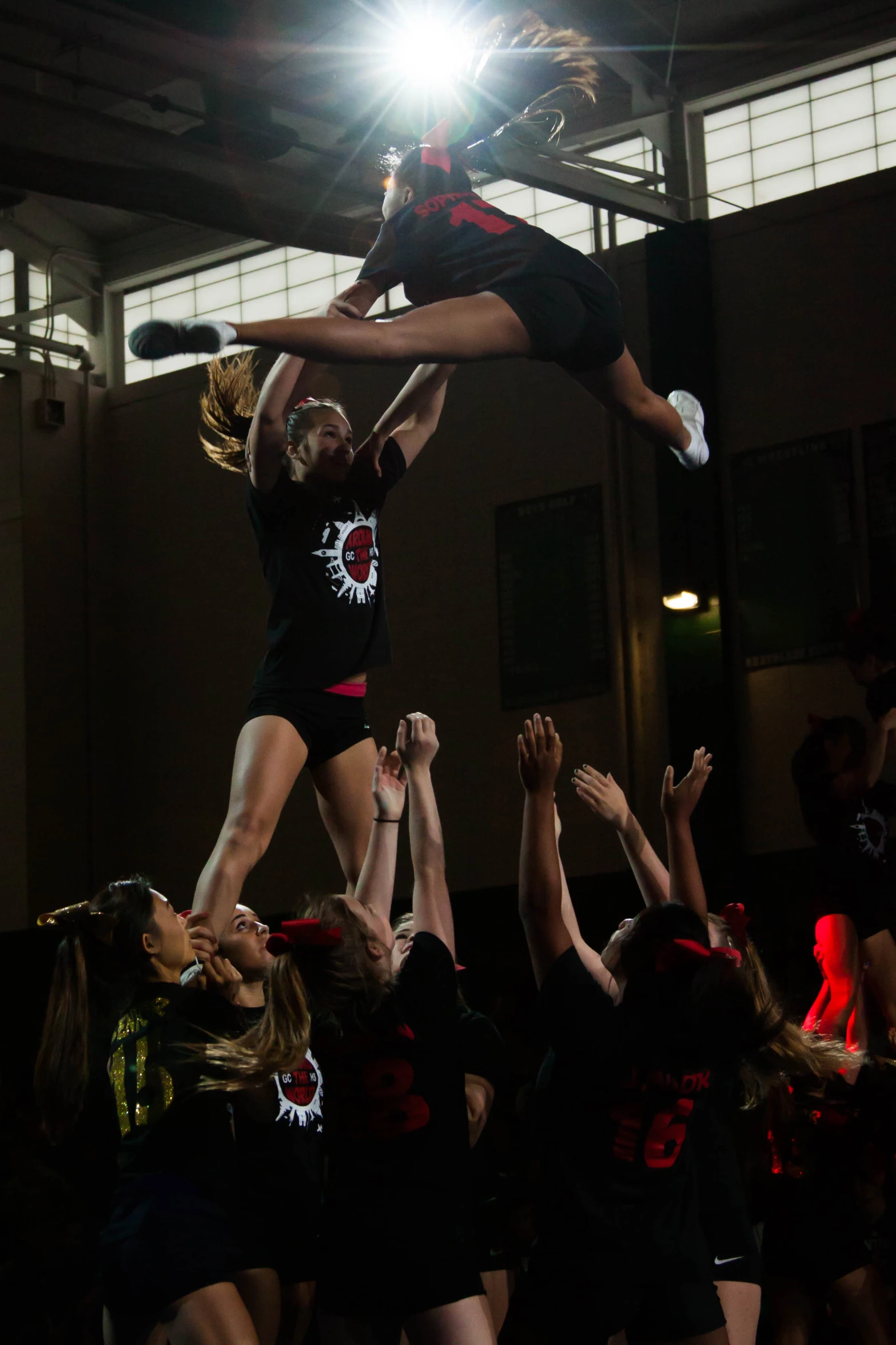 group of girls in cheerleader shirts in a gym doing a stunt