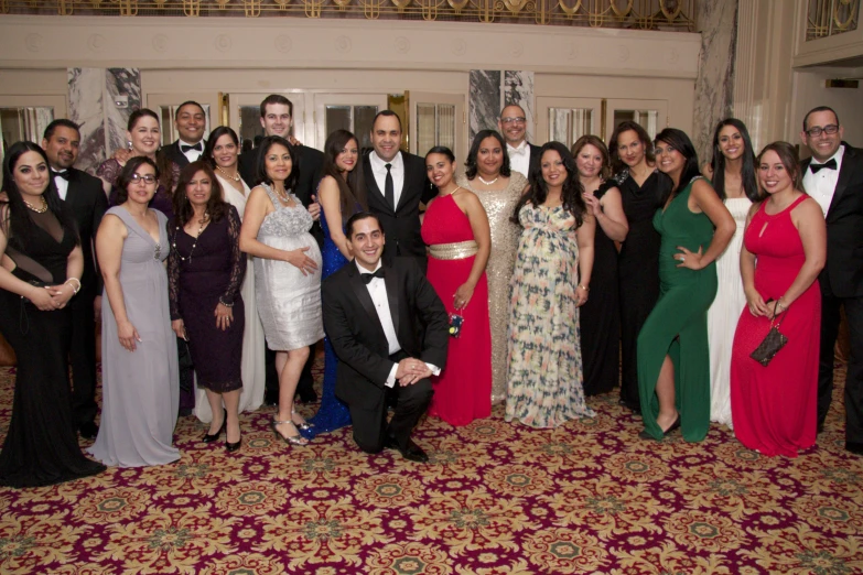 a large group of formal people in dress clothes standing in a ballroom